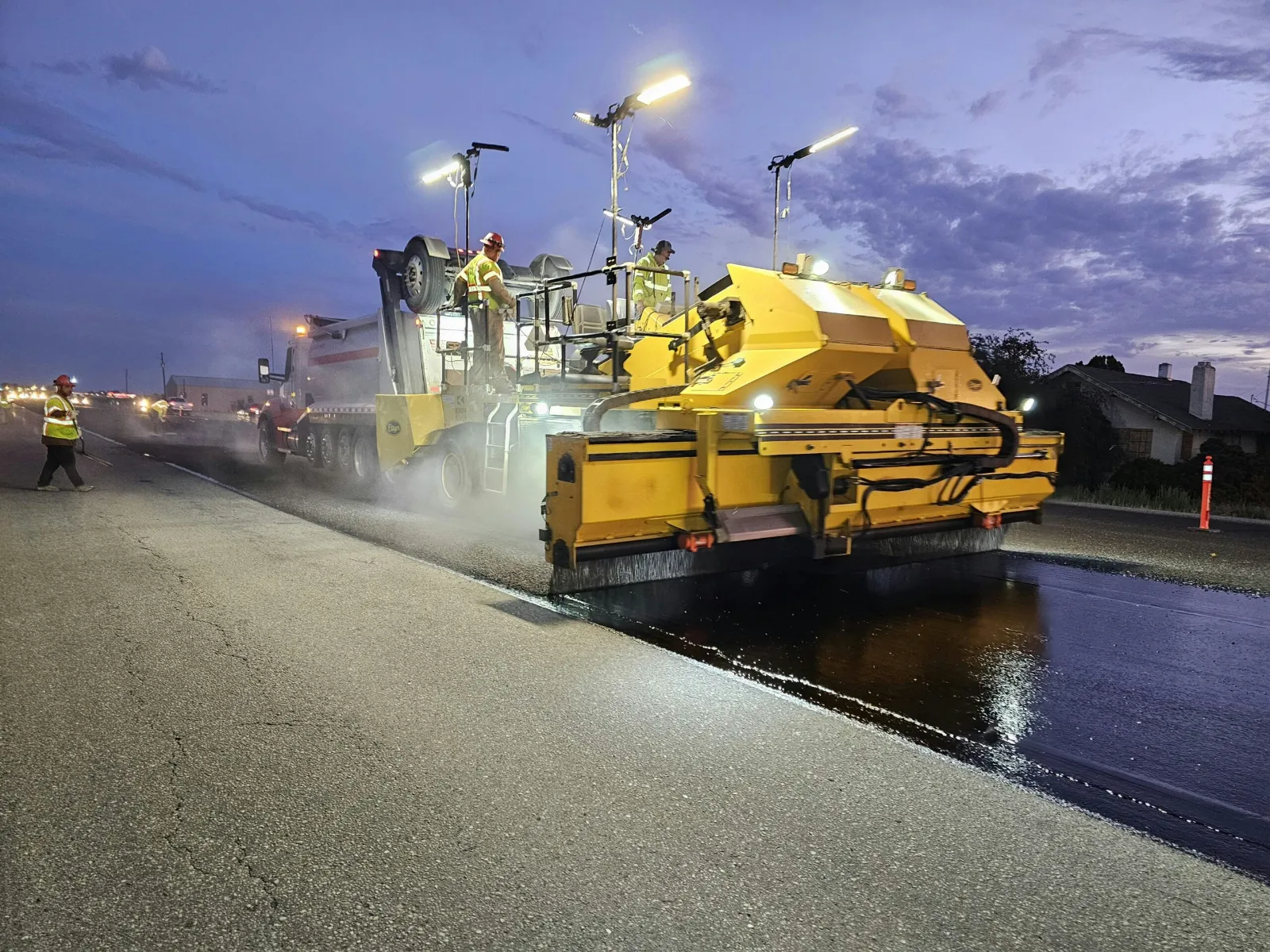 Asphalt paving machine laying new pavement at dusk